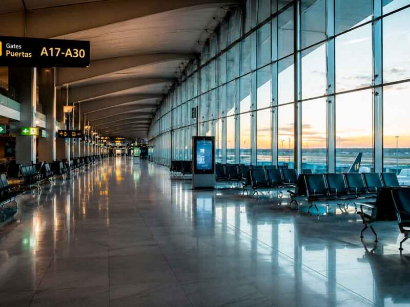 Interior de una terminal de aeropuerto internacional con zona de embarque y grandes ventanales.
