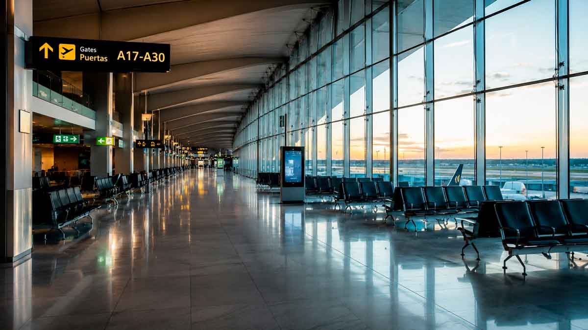 Interior de una terminal de aeropuerto internacional con zona de embarque y grandes ventanales.